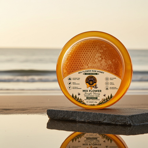 A round jar of Mix Flower Raw Honey with a visible honeycomb piece inside, set on a dark stone slab at the edge of a beach with the ocean and sky in the background.